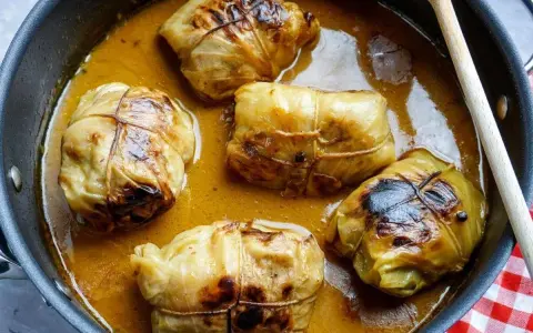 Fünf Kohlrouladen im Topf, bereit für ein köstliches Kohlrouladen Rezept. Eine Holzspatel liegt daneben.