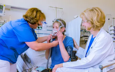 Ärztin und Pflegekraft helfen Patientin mit Lungenemphysem bei der Anpassung einer Beatmungsmaske. Medikamente sind Teil der Behandlung.