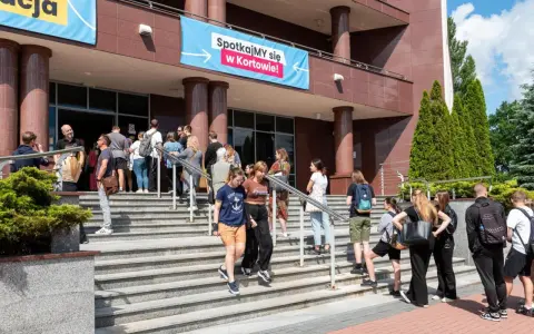Grupa młodych ludzi schodzi po schodach przed budynkiem, gdzie wisi baner "Spotkajmy się w Kortowie!". To idealne miejsce na rozpoczęcie studiów w Olsztynie.