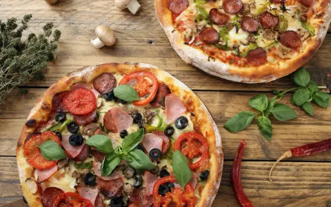 Dwie pizze z dodatkami: salami, pomidory, oliwki, szynka, pieczarki i bazylia.