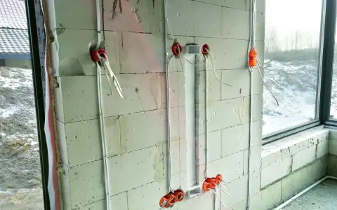 Instalacja elektryczna w ścianie z bloczków betonowych, etap prac wykończeniowych od stanu surowego zamkniętego. Widoczne puszki i przewody.
