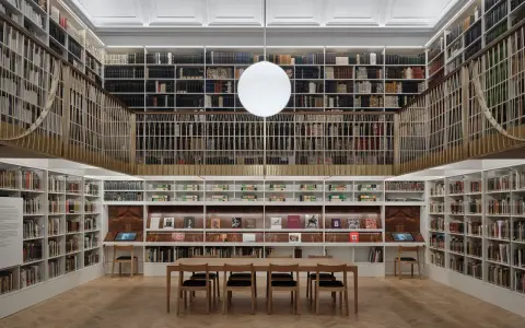 A grand library with towering bookshelves, a central reading table, and a modern globe light. This space feels like a capital photography center for learning.