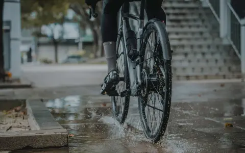 Rowerzysta w deszczu, koła rozpryskują wodę. Montaż błotnika rowerowego zapewnia suchą jazdę.