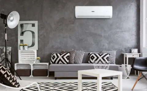 Un moderno soggiorno con divano grigio, cuscini geometrici e un **condizionatore** a parete. Il significato è comfort e stile.