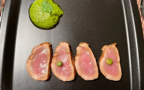 Cuatro lonchas de tataki de salmón con un toque de verde y una guarnición vibrante.