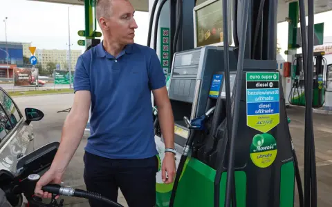 Mężczyzna dokonuje tankowania swojego samochodu na stacji paliw. W ręku trzyma pistolet do paliwa, gotowy do rozpoczęcia procesu.