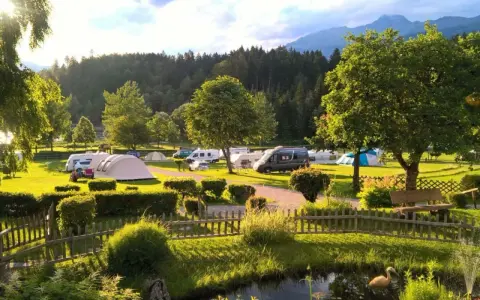 Idyllischer Campingplatz in den Dolomiten mit Wohnmobilen, Zelten und einem Teich.