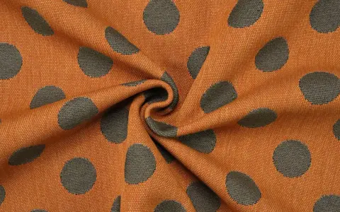 Orangefarbener Stoff mit dunklen Punkten, die wie kleine Kreise aussehen. Das Muster ist unregelmäßig und wirkt lebendig.