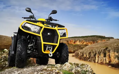 Un quad amarillo listo para conducir por terrenos escarpados junto a un río.