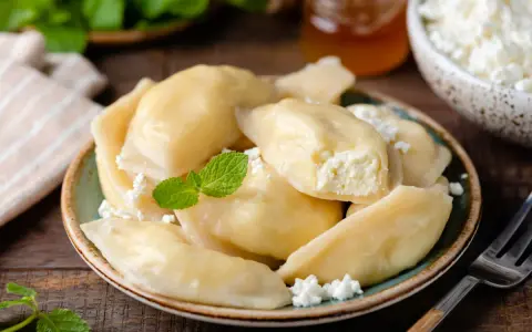 Pyszne pierogi z serem, udekorowane miętą i posypane białym serem. Obok słoiczek miodu i miseczka z serem.