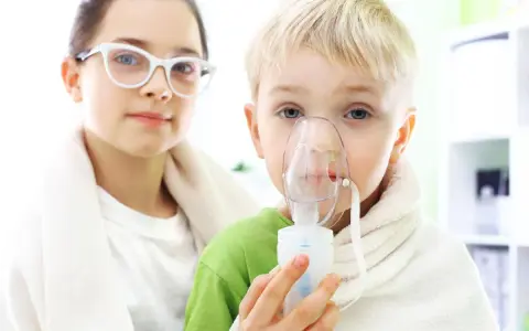 Dziecko z maską inhalatora, obok dziewczynka w okularach.