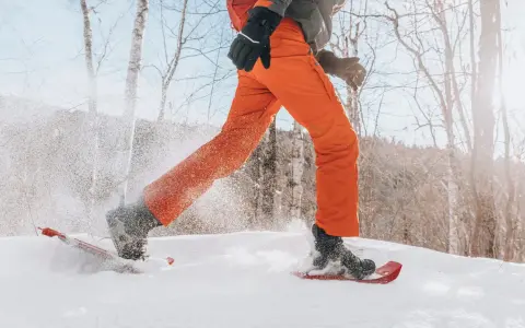 Person beim Schneeschuhwandern, die mit ihren speziellen Schuhen durch tiefen Schnee stapft.
