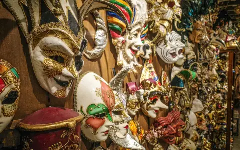 Una parete piena di maschere di carnevale romane, riccamente decorate, pronte per un ballo in maschera.