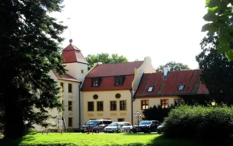 Zamek z czerwoną wieżą i dachami, otoczony zielenią. Samochody zaparkowane na trawniku. Idealne miejsce na krokowa atrakcje.