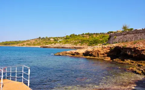 Scogliera rocciosa e mare cristallino a San Gregorio Salento, con una terrazza in primo piano.