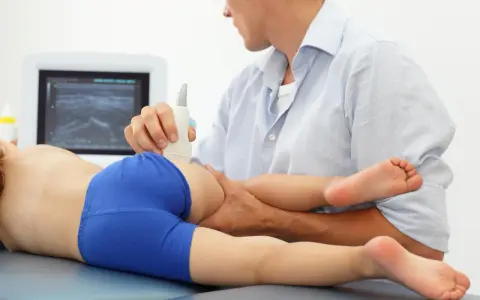 Lekarz wykonuje USG bioder u dziecka, diagnozując zapalenie stawu biodrowego.