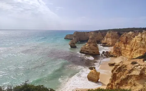 Acantilados dorados y mar turquesa en la ruta de los siete valles colgantes. Olas rompen en la arena de una playa escondida.
