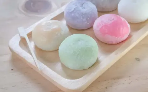 Kolorowe mochi na drewnianej tacce. Chcesz wiedzieć, jak zrobić mochi? Te słodkie kuleczki wyglądają pysznie!