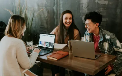 Trzy kobiety śmieją się przy laptopach, pracując nad wspólnym projektem. To idealna prasówka z WOS-u, pełna pozytywnej energii i współpracy.