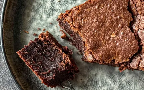 Pyszne, wilgotne brownie bezglutenowe na popękanym, szarym talerzu. Kawałek z widelcem czeka na spróbowanie.