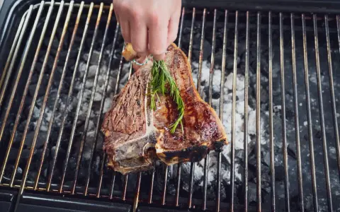 Ein saftiger florentiner steak wird mit Rosmarin auf dem Grill verfeinert.