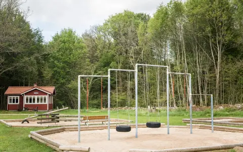 Lekplats med gungor och sandlåda vid en röd stuga, en idyllisk plats som påminner om nyrups naturhotell.