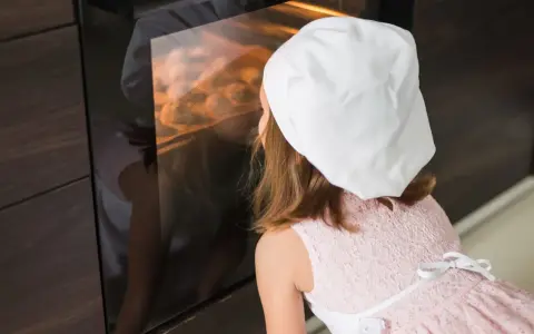 Niña con gorro de chef mirando dentro de un horno encendido.