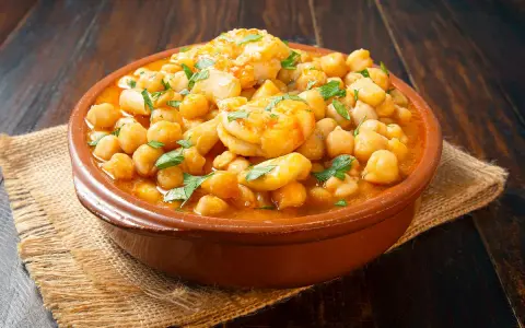 Un plato de barro con garbanzos y langostinos, adornado con perejil fresco, sobre una mesa de madera rústica.