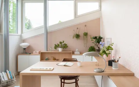 Une petite chambre avec bureau, lumineuse et décorée de plantes. Le bureau en bois clair est prêt pour le travail ou la lecture.