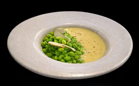 Un plato de guisantes de lágrima frescos con una cremosa sopa amarilla y una fina lámina de champiñón.