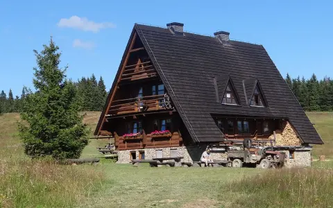 Drewniana bacówka na Krawcowym Wierchu, otoczona zielenią i lasem. Obok stoi stary traktor.