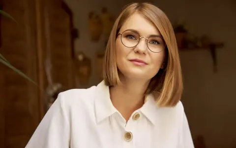 Kobieta w białej koszuli z guzikami, nosząca okulary w cienkich oprawkach, patrzy wprost.