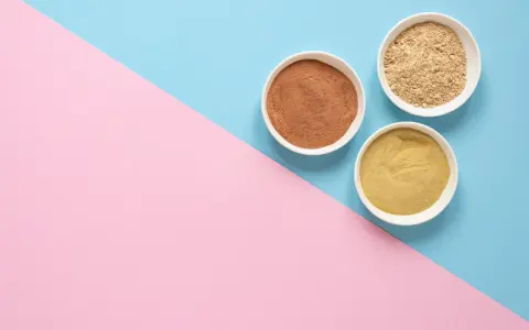 Tres cuencos blancos con polvos de diferentes tonos, como masilla para pared interior, sobre un fondo dividido en rosa y azul.