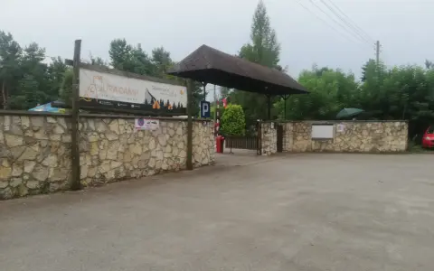 Wjazd na siamoszyce camping przez kamienny mur. Baner "Jura Camp" zaprasza do wypoczynku wśród drzew.
