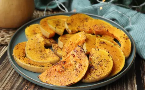 Rodajas de calabaza a la plancha, doradas y especiadas, servidas en un plato azul sobre una mesa de madera.