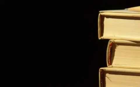 Libri impilati, un libro in cima con una matita. La luce crea ombre, un po' come l'anastrofe figura retorica che inverte l'ordine per enfasi.
