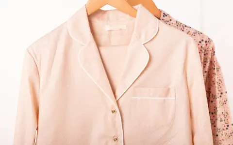 Pyjama rose à pois blancs, col rabattu, suspendu sur un cintre en bois. Une autre chemise à fleurs est visible derrière.