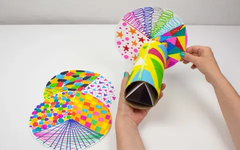 Manos creando manualidades con material reciclado para adolescentes: un caleidoscopio con tubos de cartón y discos decorados con patrones coloridos.