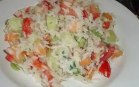 Une savoureuse salade de riz garnie de dés de tomates, de concombre et d'herbes fraîches, servie sur une assiette blanche.