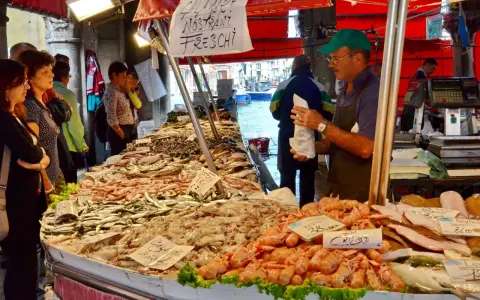 Mercato del pesce a Venezia: bancarelle piene di pesce fresco, gamberi e calamari. Un venditore serve i clienti.