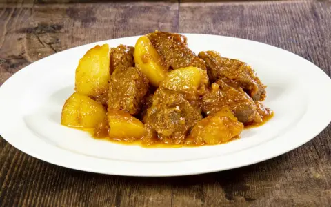 Un saporito spezzatino di vitello con patate, servito su un piatto bianco, su uno sfondo di legno scuro.