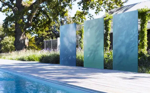 Ausgefallener Sichtschutz Garten selber machen: Vertikale, blaue und grüne Metallplatten vor üppiger Bepflanzung und Pool.