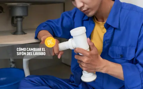 Un fontanero realiza la instalación del sifón del lavabo, sujetando la pieza blanca con ambas manos.