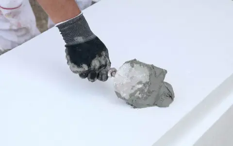 Ręka w rękawicy nakłada zaprawę na styropian. To pokazuje, jaki klej do styropianu wybrać do prac termoizolacyjnych.