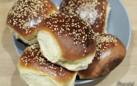 Pięć puszystych bułek do burgerów, posypanych sezamem, ułożonych na talerzu. Idealne na domowe burgery.