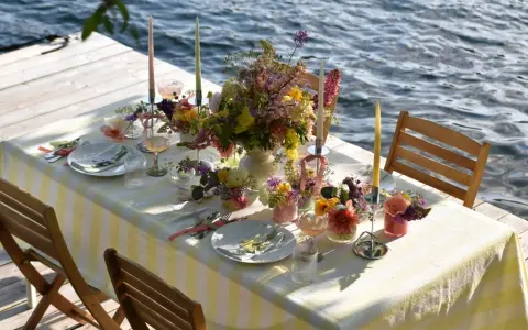 Enkel dukning vid vattnet med blommor och ljus.