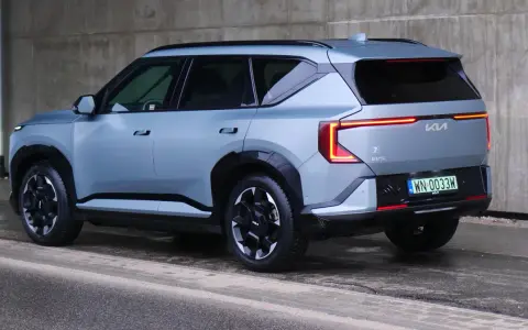Nowoczesne kia ev5 w kolorze jasnoszarym, z charakterystycznymi tylnymi światłami, zaparkowane przy betonowej ścianie.