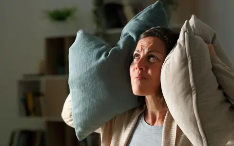 Donna con cuscini sulle orecchie, infastidita da un rumore. Un esempio di 35 decibel, come un sussurro, può disturbare.