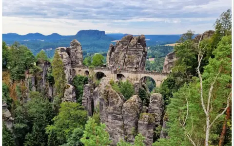 Kamienny most Basteibrücke w Szwajcarii Saksońskiej, łączący skalne baszty pośród zielonych lasów i gór.