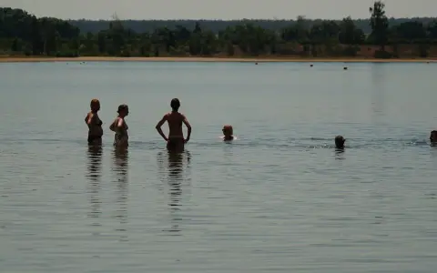 Menschen genießen das naturbad luppa an einem sonnigen Tag. Einige stehen im Wasser, andere schwimmen.